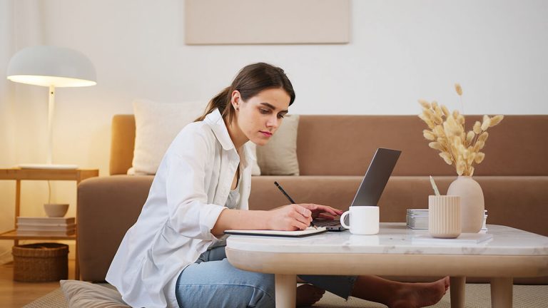 Junge Frau macht sich vor Laptop sitzend Notizen