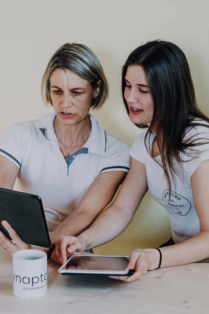 Zwei Frauen in weißen T-Shirts schauen auf den Bildschirm eines Tablets