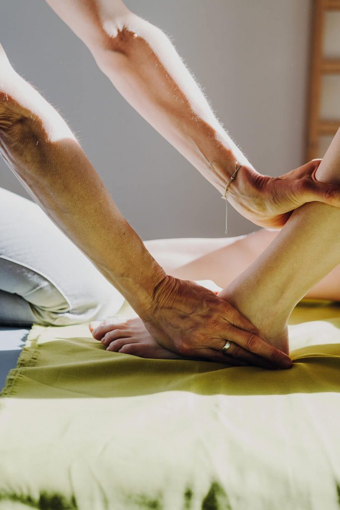 Physiotherapeutin behandelt Patientin mit Handgriffen an Wade und Fuß