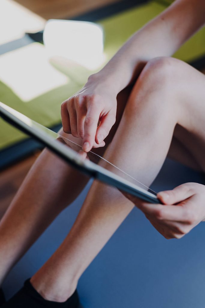 Frau mit angewinkelten Beinen tippt mit Zeigefinger auf Bildschirm eines Tablets