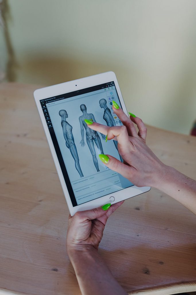 Frau mit grünen Nägeln tippt auf Tablet mit Körperkarte von synaptos
