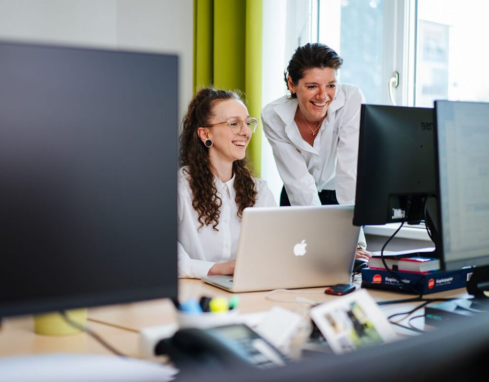 Zwei Frauen in weißen Blusen blicken auf Computerbildschirme