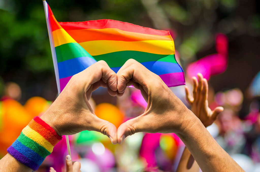 Herz geformt mit Händen vor Regenbogenflagge LGBTQIA