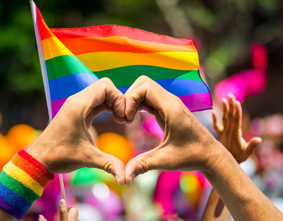 Herz geformt mit Händen vor Regenbogenflagge LGBTQIA